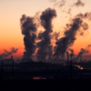 Silhouette of a factory with smoke emissions against a vibrant sunset sky.