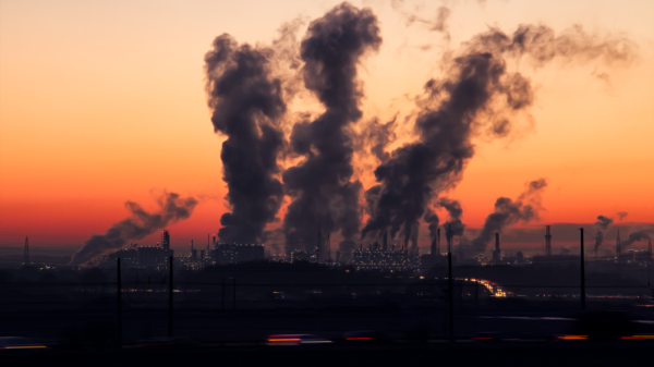 Silhouette of a factory with smoke emissions against a vibrant sunset sky.