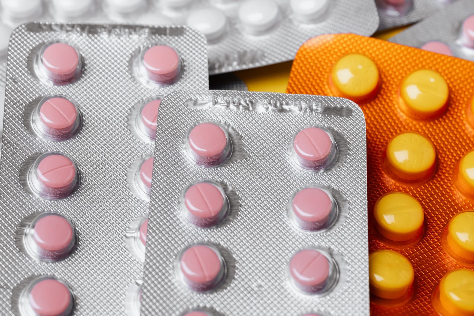 From above closeup of various multicolored pills of different sizes in plastic blister packs placed together under bright light