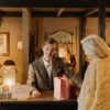 A cheerful shopkeeper assists a customer during a festive sale event in a cozy store setting.