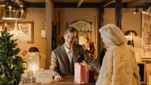 A cheerful shopkeeper assists a customer during a festive sale event in a cozy store setting.