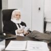 Elderly businessman relaxing at desk, counting money notes in a modern office setting.