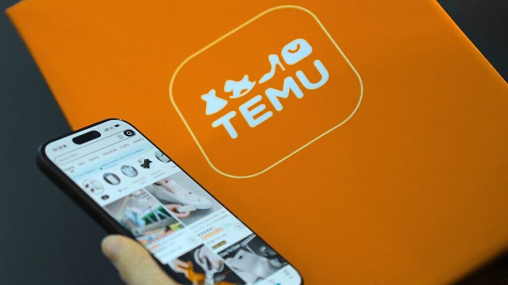 Hand holding smartphone with Temu app beside orange Temu package.