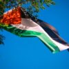 Vibrant Palestinian flag waving against a clear blue sky, representing freedom and patriotism.