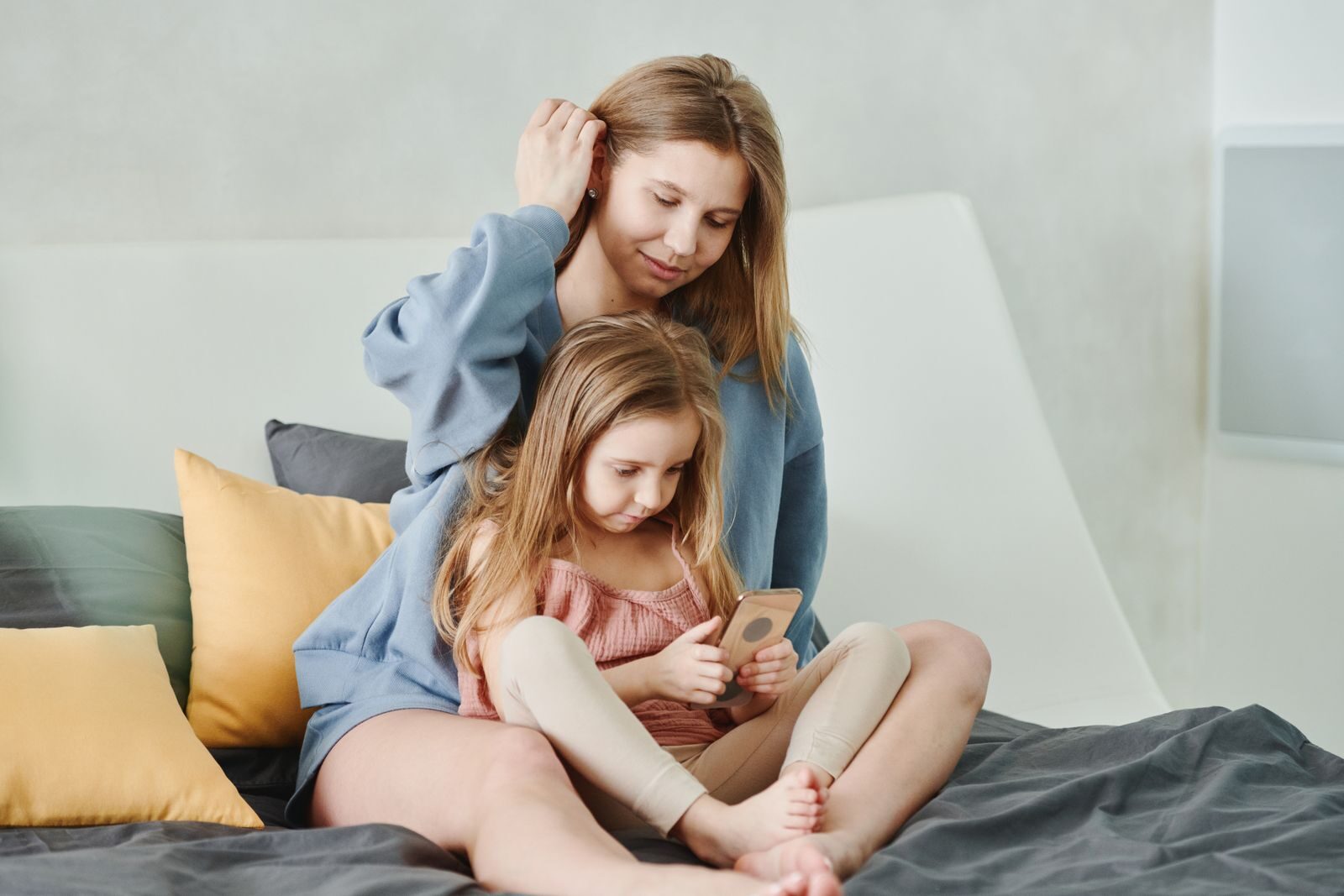 A mother and daughter spending quality time together, sitting on a cozy bed indoors.