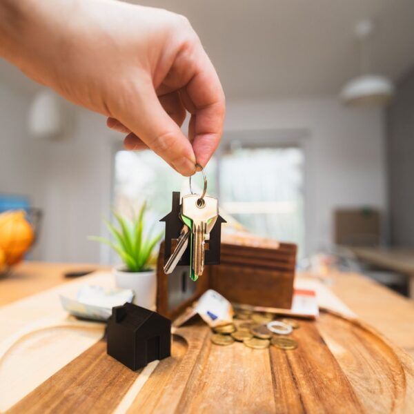 Hand holding keys in a modern living room setting, symbolizing home ownership or real estate investment.