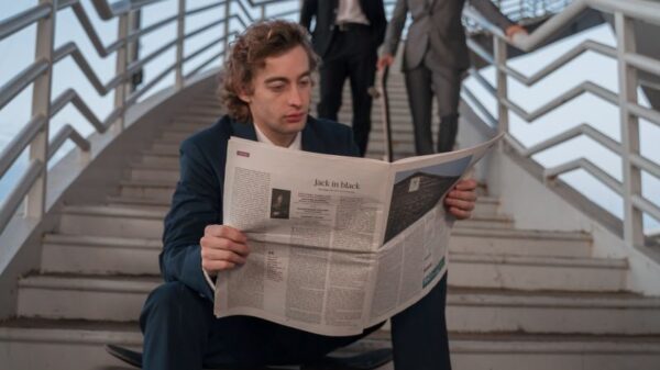 Young professionals in suits, one reading a newspaper on stairs outdoors.