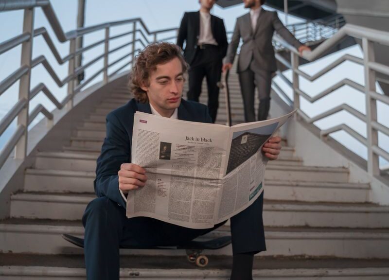 Young professionals in suits, one reading a newspaper on stairs outdoors.