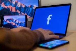 Laptop displaying Facebook at workspace with multiple devices, highlighting modern technology.