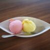 Delicious strawberry and lemon ice cream scoops served in a white bowl with a spoon on wooden table.