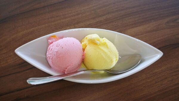 Delicious strawberry and lemon ice cream scoops served in a white bowl with a spoon on wooden table.