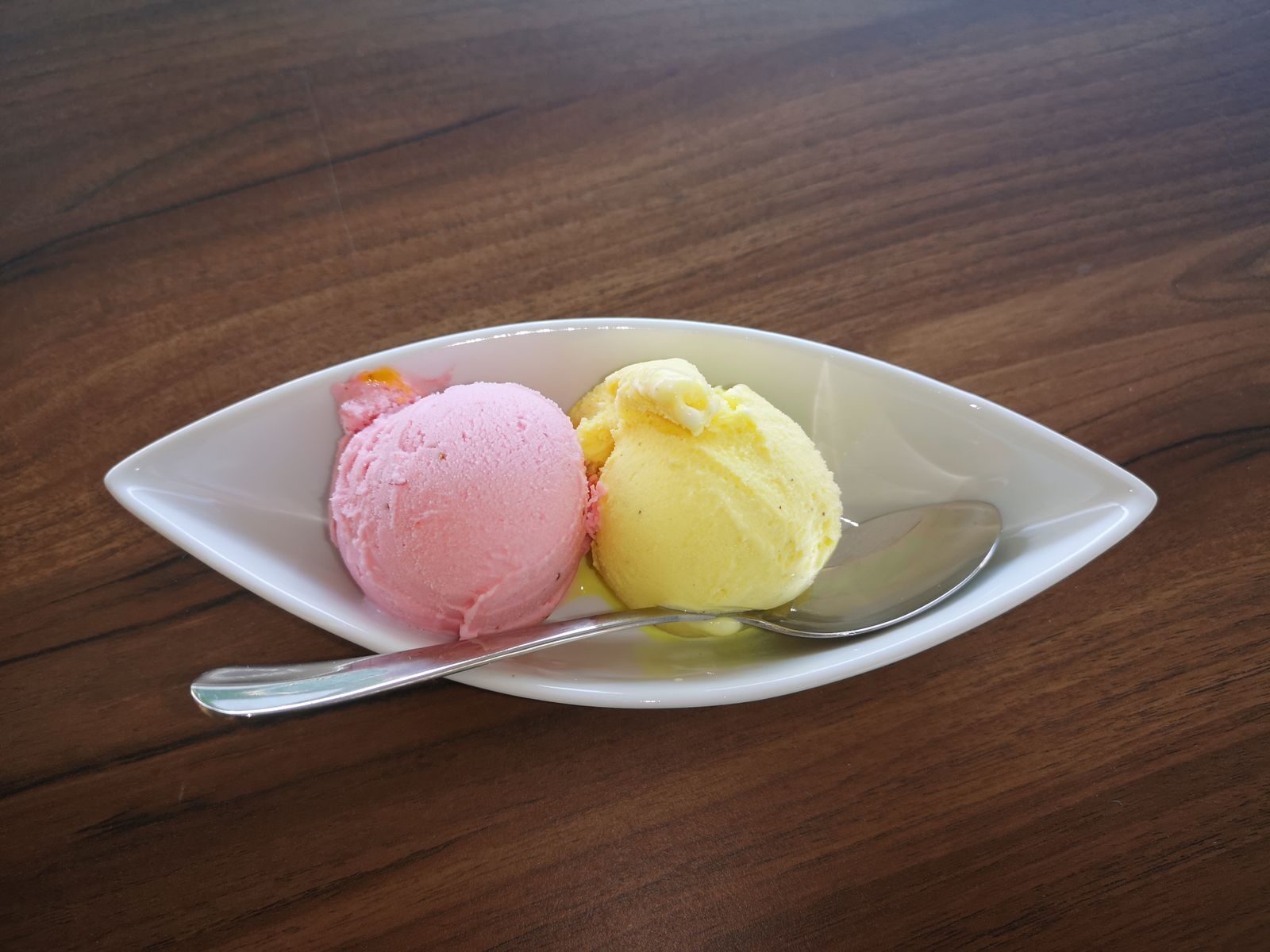 Delicious strawberry and lemon ice cream scoops served in a white bowl with a spoon on wooden table.