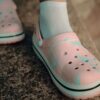 Detailed view of pink Crocs worn with white socks on a textured surface.