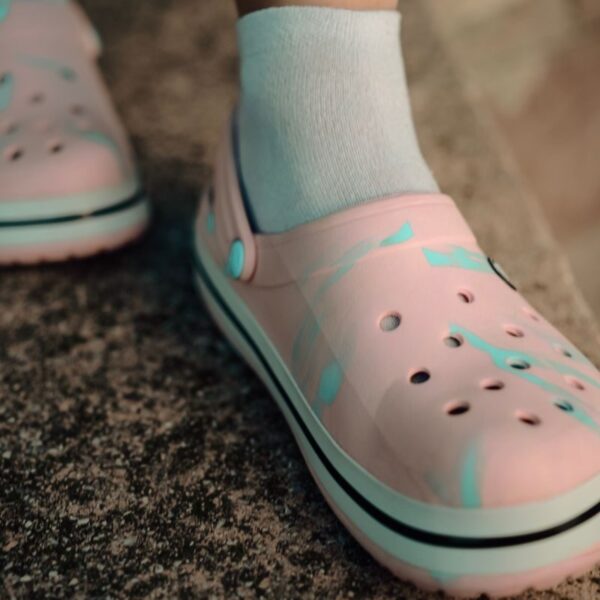 Detailed view of pink Crocs worn with white socks on a textured surface.