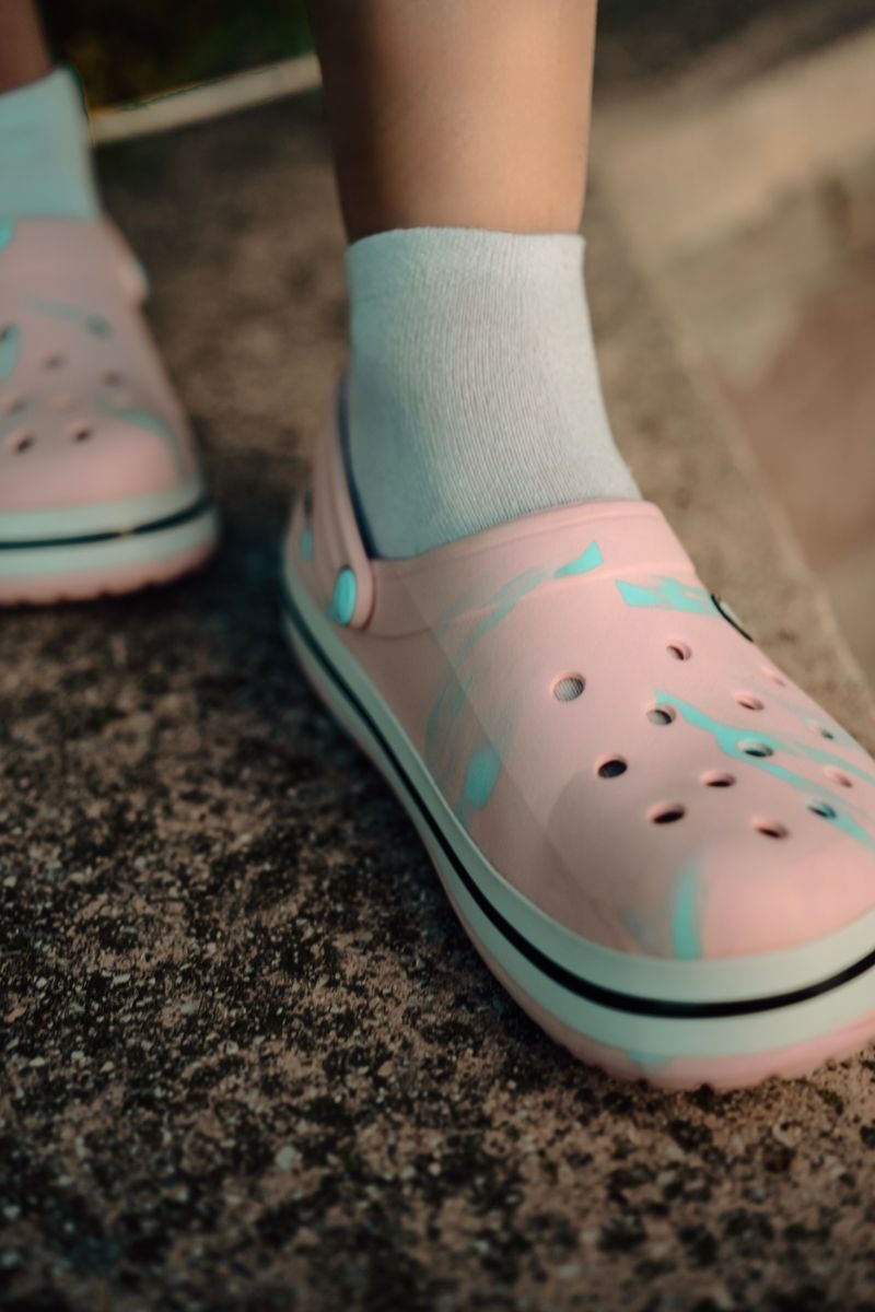 Detailed view of pink Crocs worn with white socks on a textured surface.