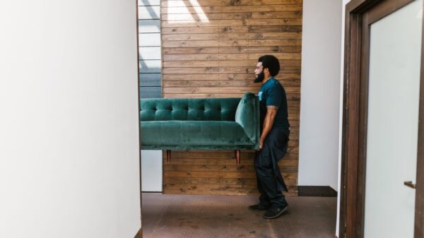 A mover carries a green sofa indoors, showcasing modern interior design and relocation services.