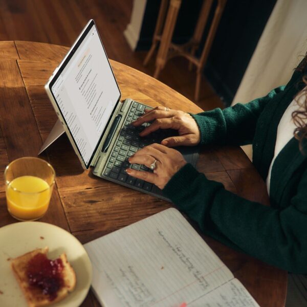 Woman typing on laptop at wooden table with breakfast.
