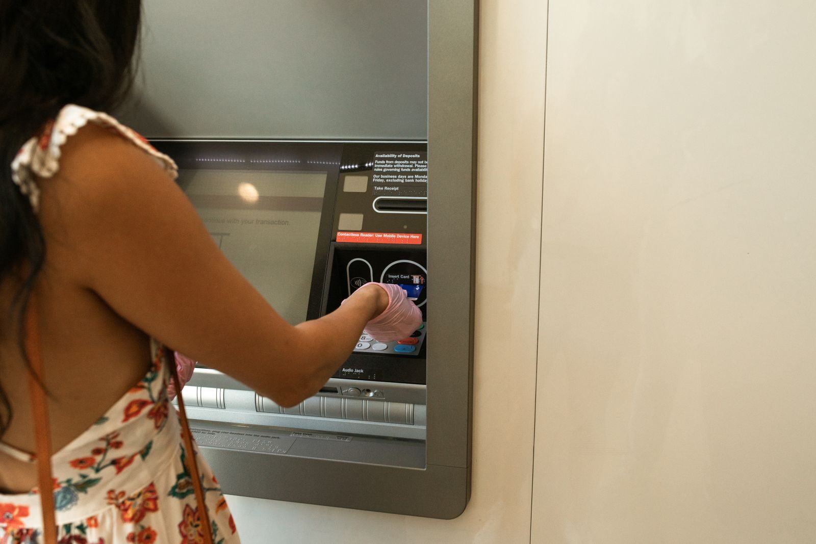 Woman using an ATM machine while wearing protective gloves indoors.