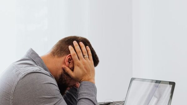 A frustrated man sits at a desk with a laptop and charts, showing work stress.