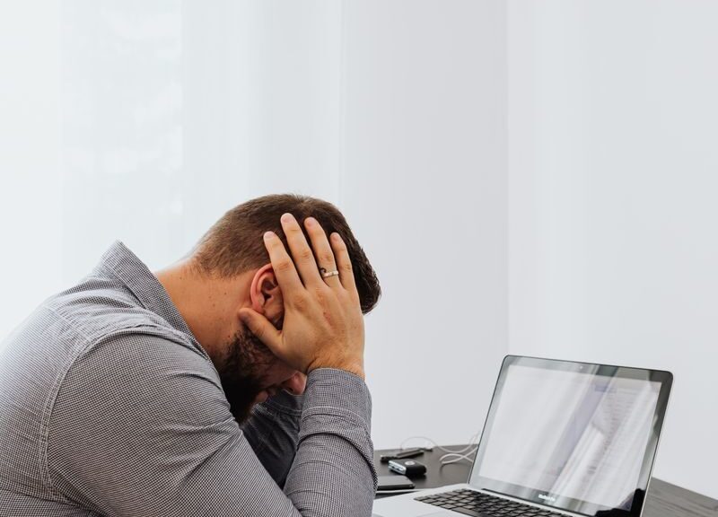 A frustrated man sits at a desk with a laptop and charts, showing work stress.