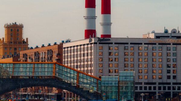 Cityscape featuring red chimneys, riverboats, and urban buildings under a clear sky.