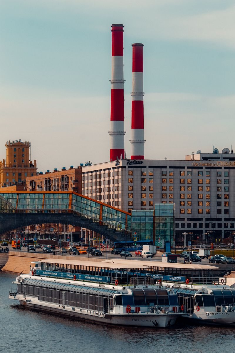 Cityscape featuring red chimneys, riverboats, and urban buildings under a clear sky.