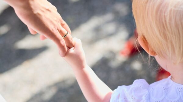 Blonde child holding parent's hand outdoors, symbolizing love and protection.
