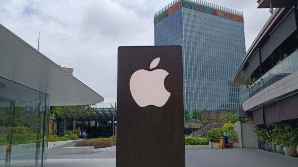 Outdoor scene featuring a tall metal structure with an Apple logo against an urban skyline.
