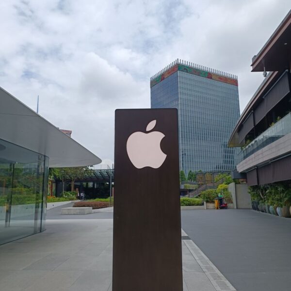 Outdoor scene featuring a tall metal structure with an Apple logo against an urban skyline.