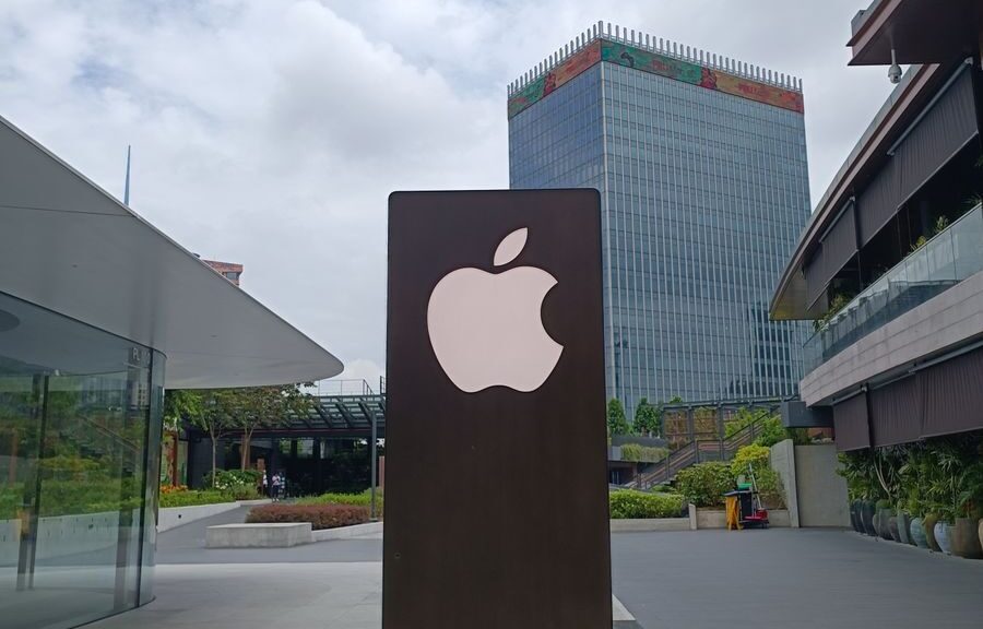Outdoor scene featuring a tall metal structure with an Apple logo against an urban skyline.