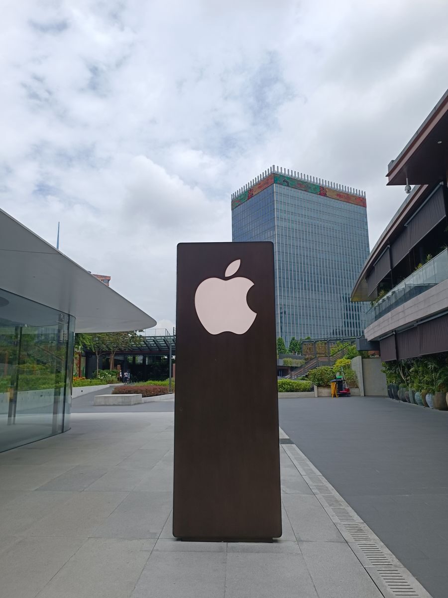 Outdoor scene featuring a tall metal structure with an Apple logo against an urban skyline.