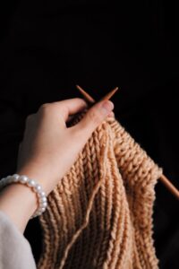 A hand knitting with wooden needles on a black background. Perfect for craft and hobby themes.
