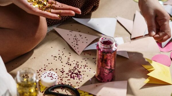 Close-up of hands crafting with colorful paper, glitter, and ribbons; perfect for DIY art projects.