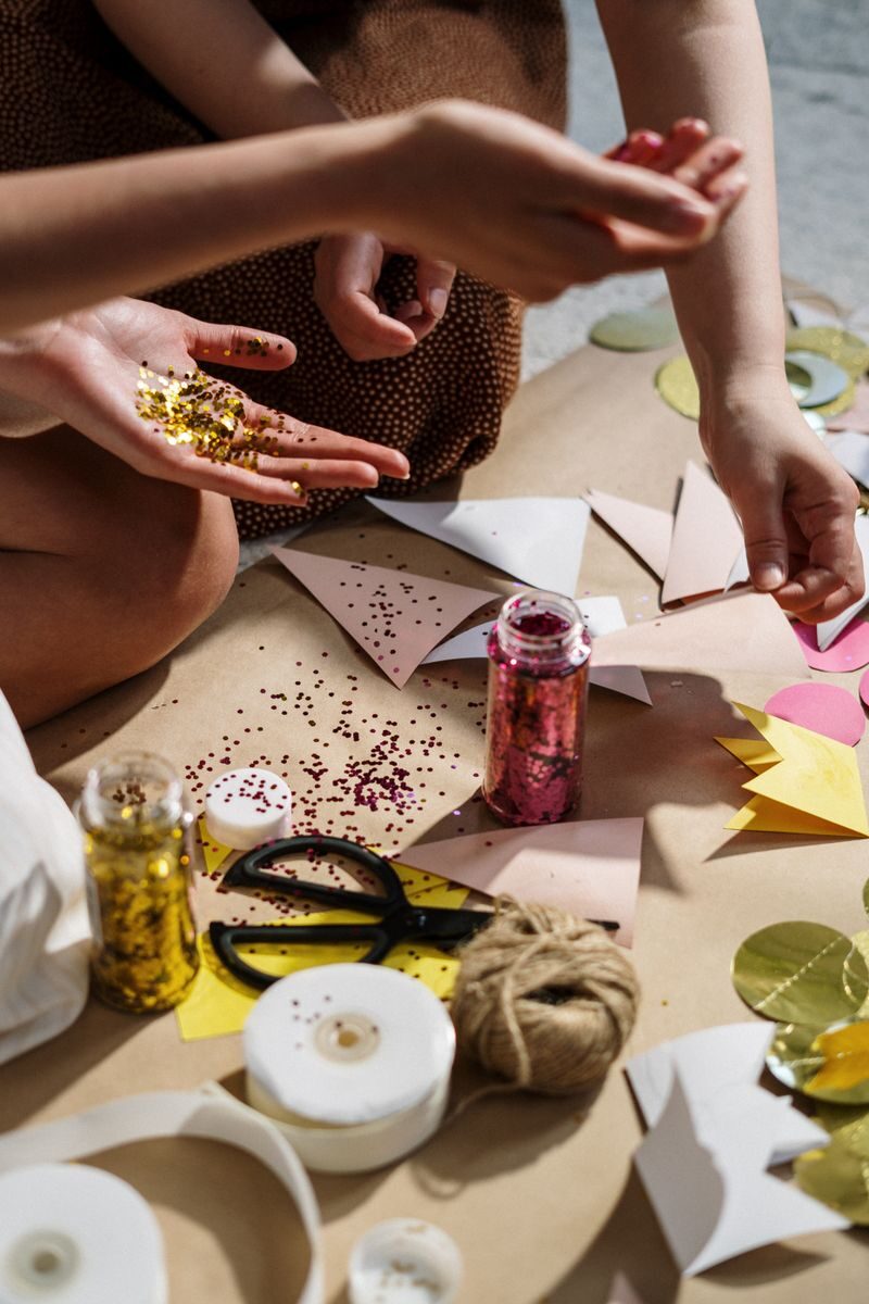 Close-up of hands crafting with colorful paper, glitter, and ribbons; perfect for DIY art projects.
