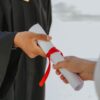 Hands exchanging a graduation diploma wrapped with red ribbon, symbolizing achievement.