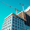 High-rise building under construction with cranes against a clear sky.