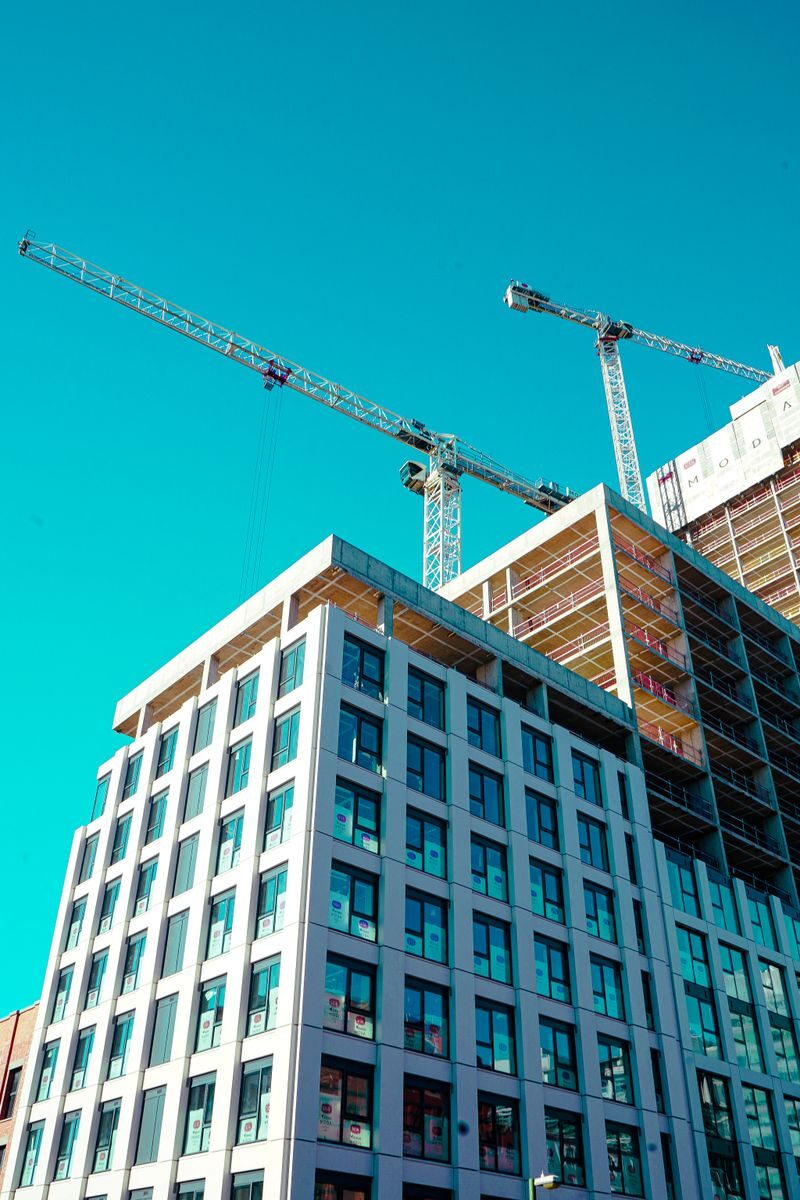 High-rise building under construction with cranes against a clear sky.