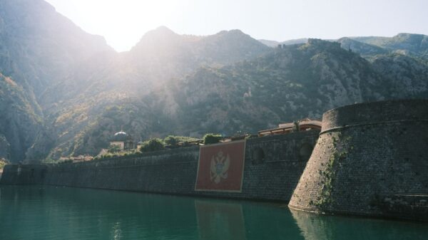 Explore the majestic Kotor fortress basking in sunlight, framed by mountains.