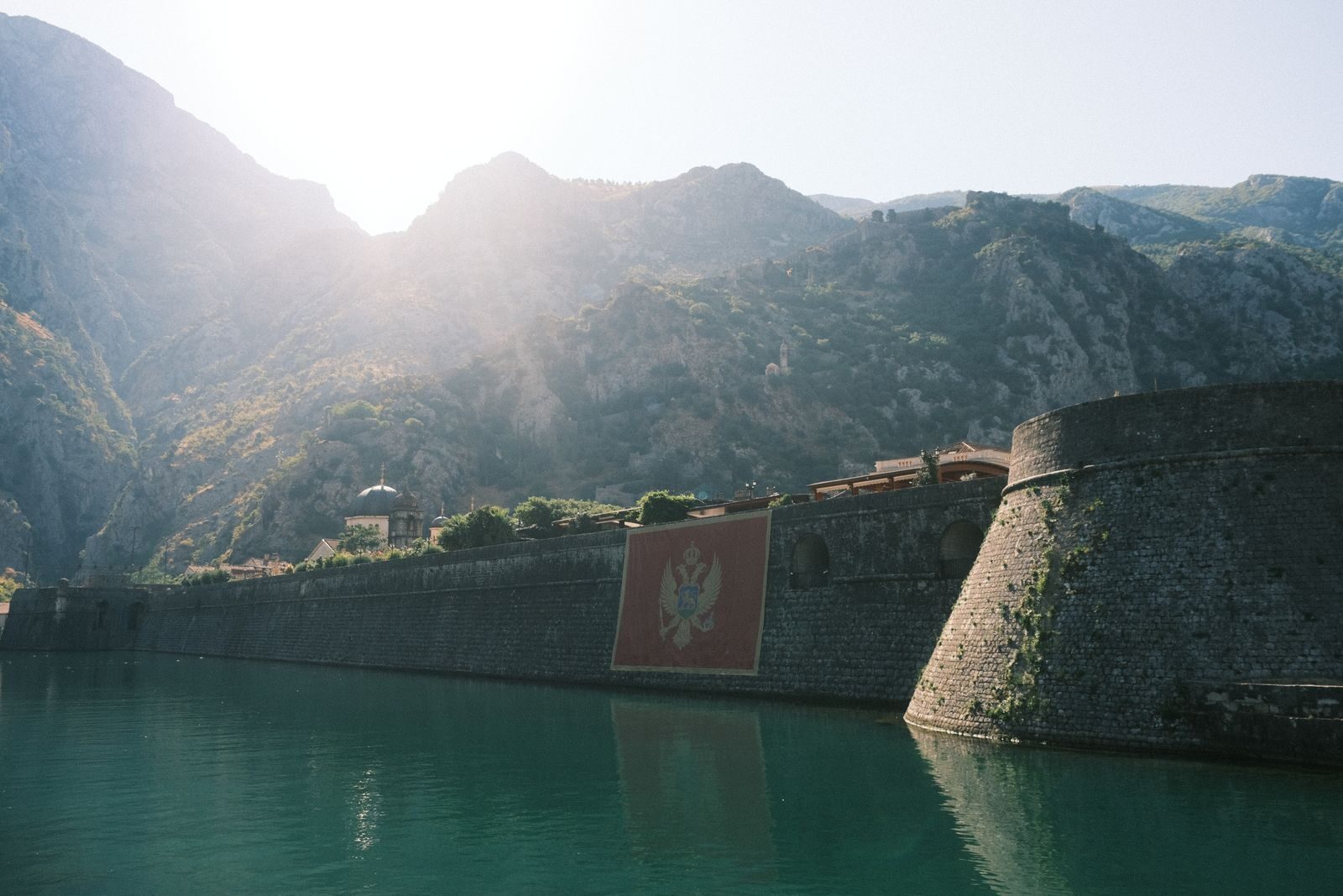 Explore the majestic Kotor fortress basking in sunlight, framed by mountains.