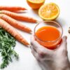 A vibrant juice with fresh carrots, ginger, and orange, captured in a studio setting.