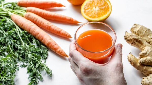 A vibrant juice with fresh carrots, ginger, and orange, captured in a studio setting.