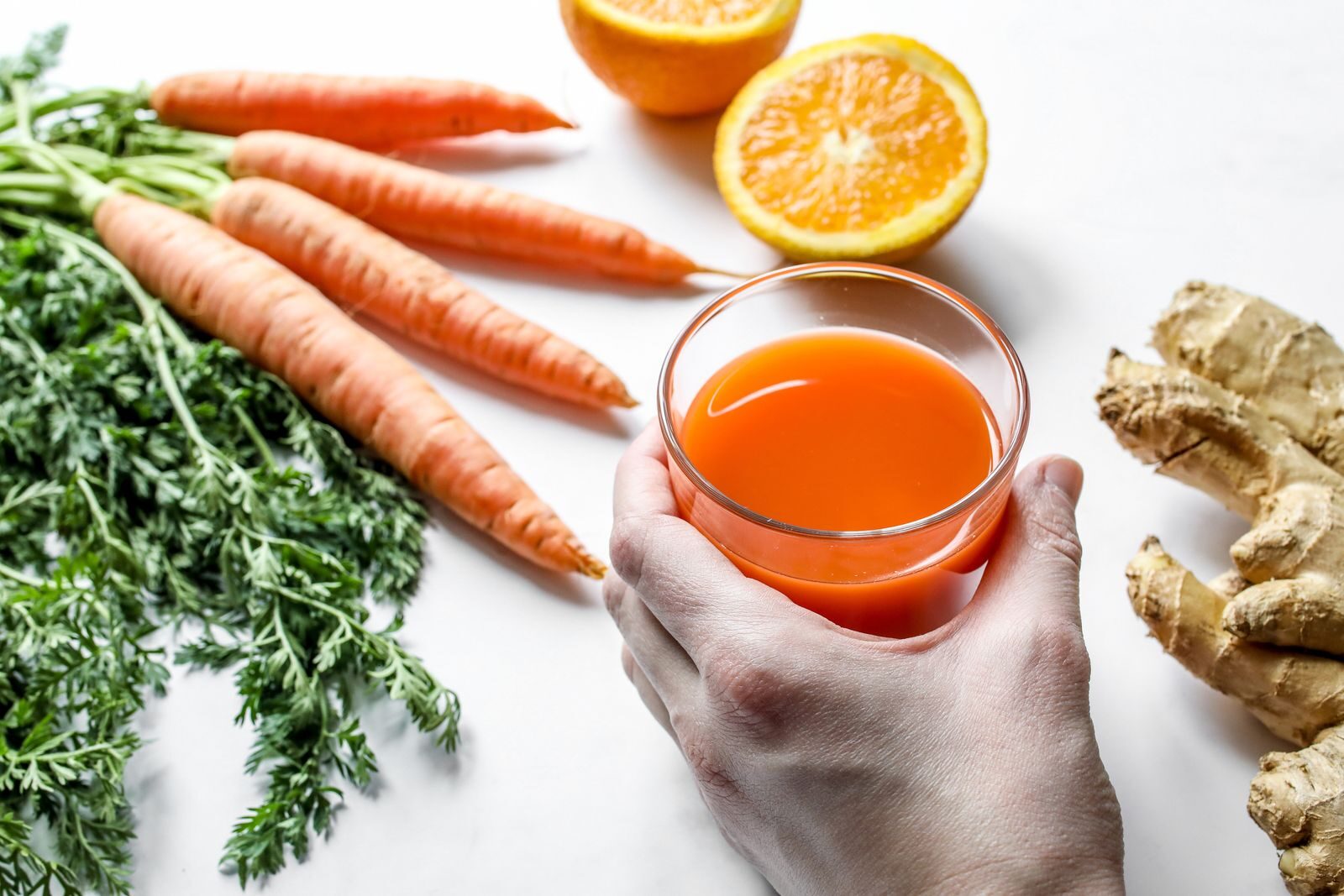 A vibrant juice with fresh carrots, ginger, and orange, captured in a studio setting.