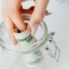 A close-up of a hand placing rolled dollars into a glass jar, symbolizing savings.