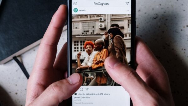 Close-up of hands holding a smartphone browsing Instagram with a notebook and pen nearby.