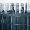 Construction workers at a high-rise building site with visible steel reinforcements.