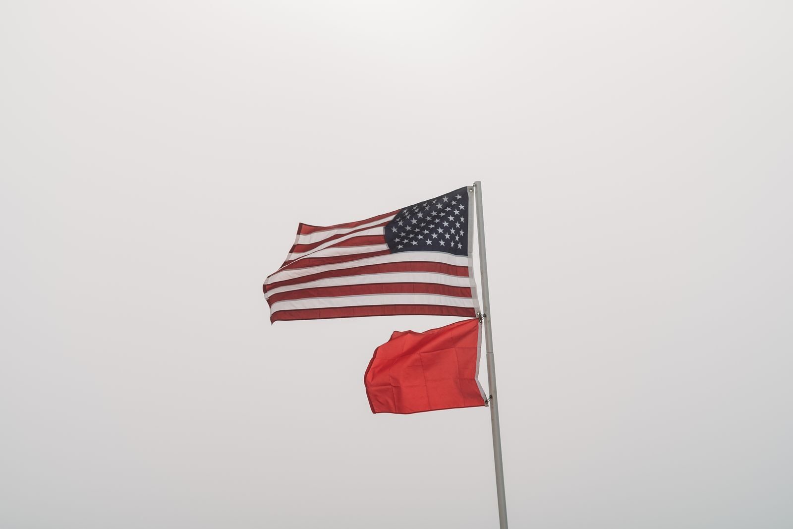 United States and warning flags on display against an overcast sky at Orange Beach, AL.