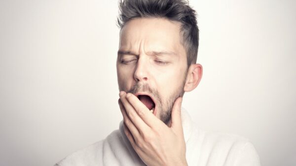 Close-up of a bearded man yawning with hand on mouth against a white background.