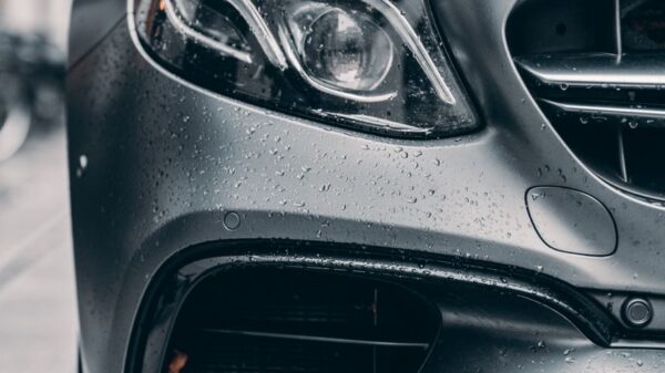 Half of front of gray car standing on city street under rain in daytime