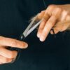 Detailed close-up of hands holding scissors, trimming hair in a salon setting.