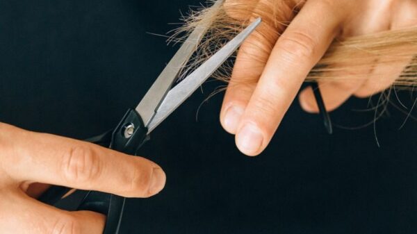 Detailed close-up of hands holding scissors, trimming hair in a salon setting.